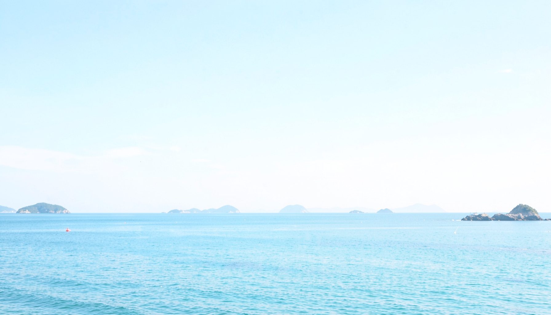 穏やかな瀬戸内海の風景、青い空と穏やかな海面、遠くに島々が浮かぶ明るい昼下がりの景色